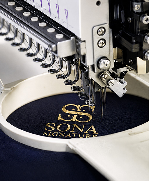 Embroidery machine stitching Sona Signature logo on navy uniform fabric